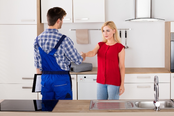 Plumber shaking hands with client in kitchen