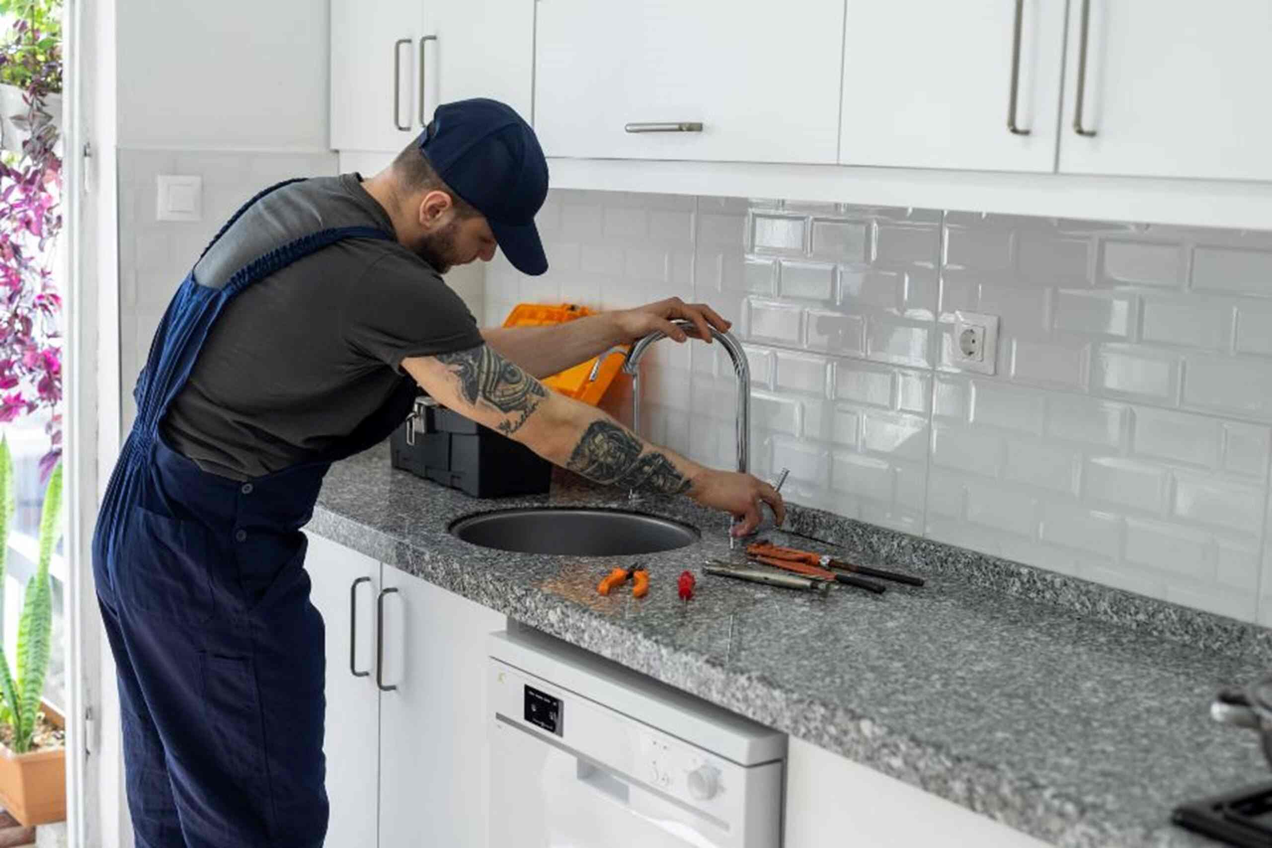A man is fixing a sink in a kitchen, providing plumbing service in Kennesaw, GA.