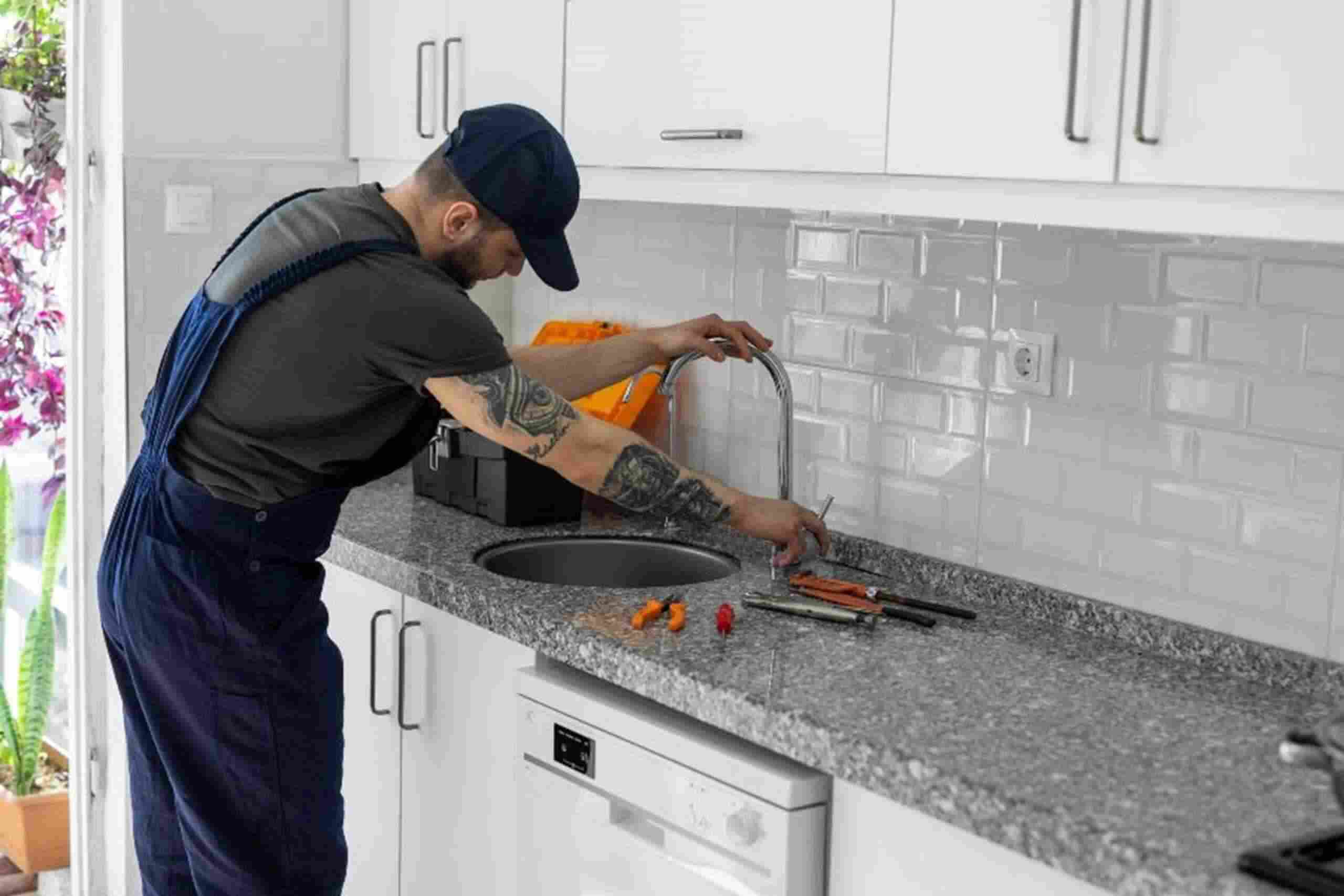 A man is fixing a sink in a kitchen, providing plumbing service in Kennesaw, GA.